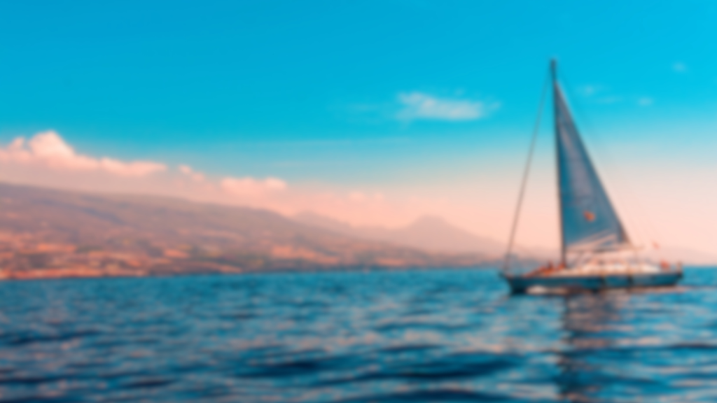 image of a sailboat on a calm sea with mountains in the background under a bright blue sky.